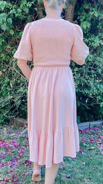 Back view of woman wearing a pastel pink smocked knee-length dress with puff sleeves outdoors