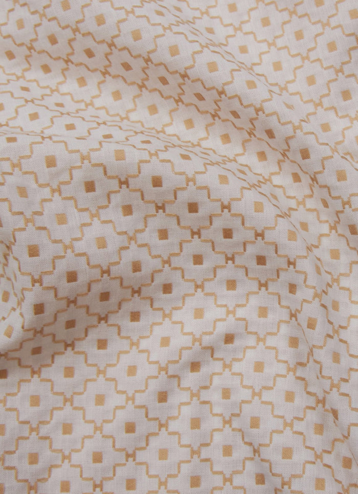 Close-up of Alimagnet fabric in light beige, showing a neutral pattern with repeating geometric diamonds and squares in light brown. Slightly wrinkled cotton material, perfect for shirts or short sleeve button downs.