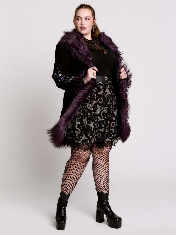 This mid-length black coat pairs a soft, suede-like finish with plush amethyst-purple faux fur trim