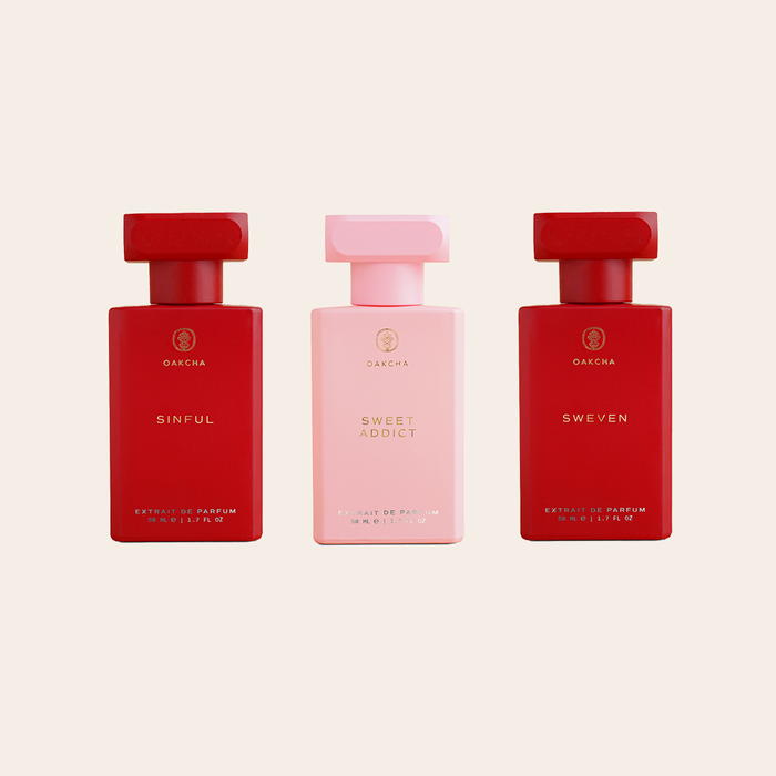 Front view of three Oakcha extrait de parfum bottles showing pink and red color variants and front labels on pale beige background
