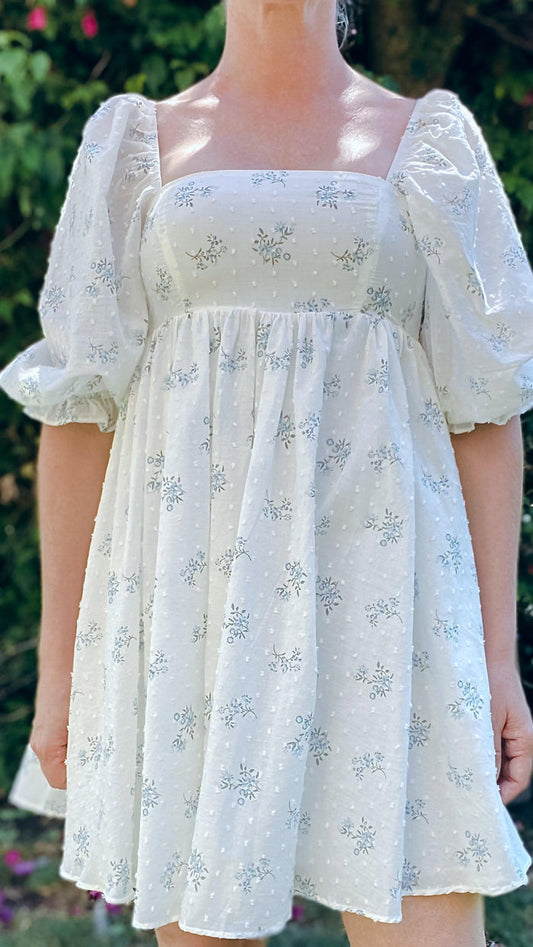 White mini dress with puff sleeves and delicate blue floral print in outdoor garden setting