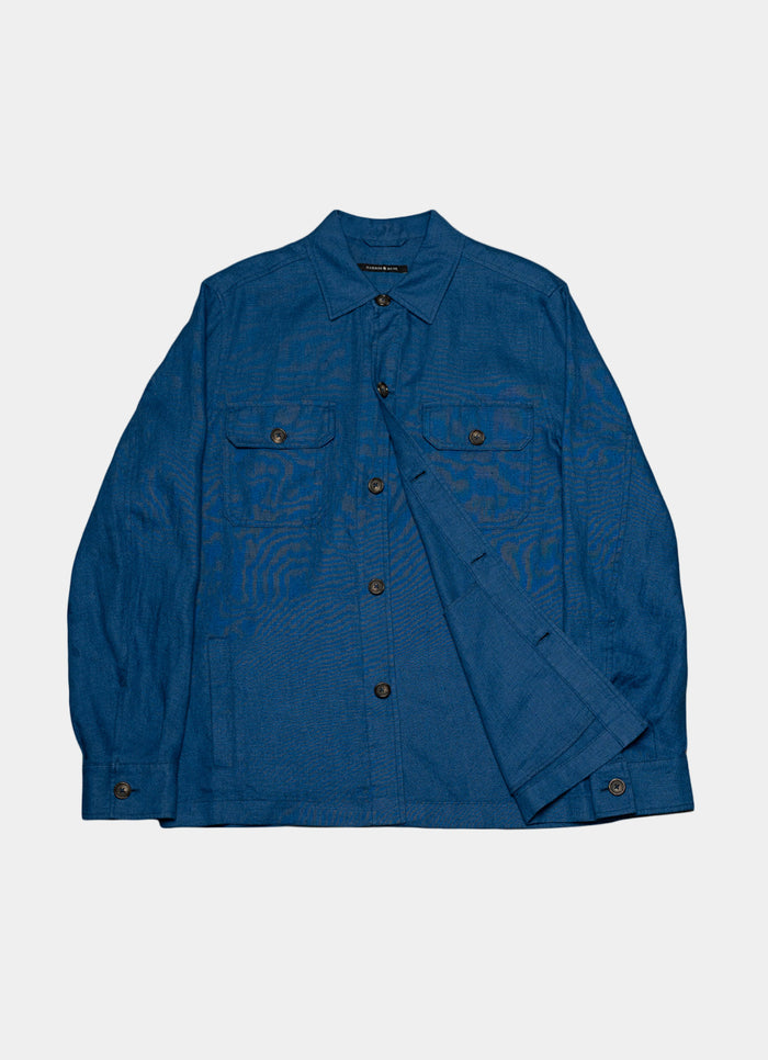 The Harbour Overshirt is a blue linen shirt with a collar, long sleeves, button front, and two flap chest pockets. Shown on a plain white background, it features a relaxed fit for effortless casual style.