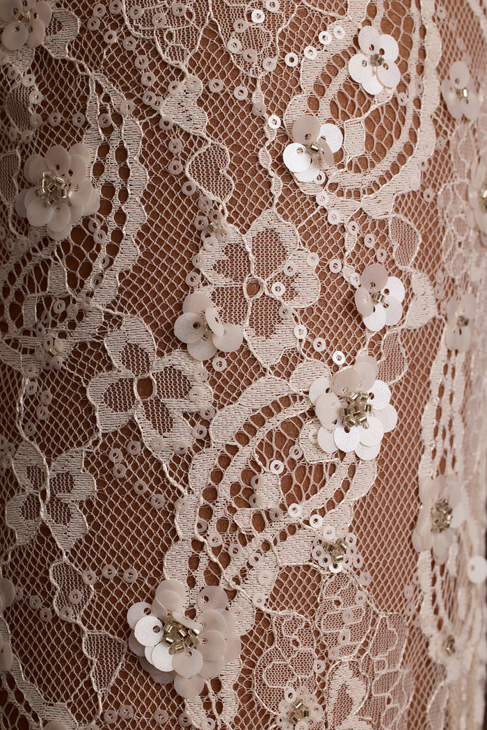 Close-up of ivory sequin lace fabric with a floral paisley pattern.