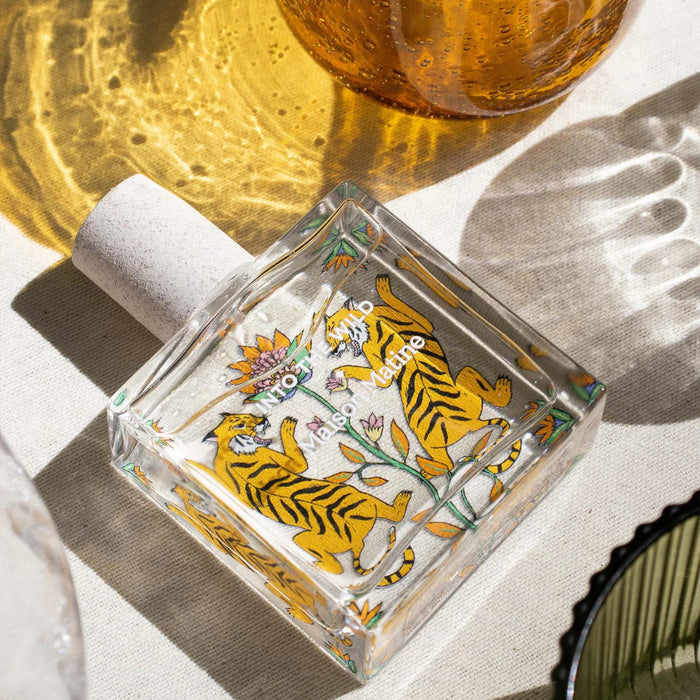 Maison Matine Into the Wild perfume bottle on a cream colored table with amber glass and a shadow.
