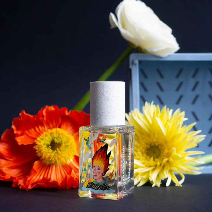 Small glass bottle with a colorful label next to flowers on a dark background