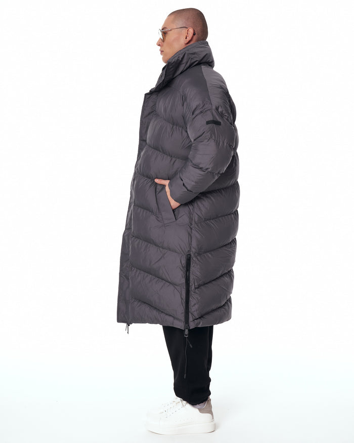 Martin Valen oversized long gray puffer coat left profile, high folded collar with hand in pocket and chunky quilted panels