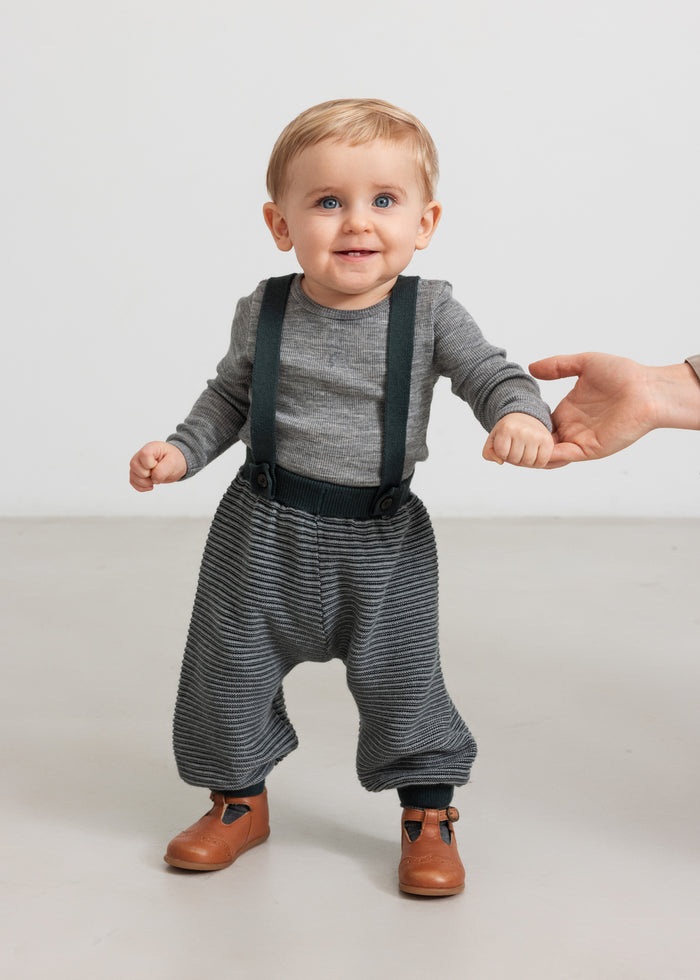 Baby wearing dark green knitted pants with suspenders and gray blouse