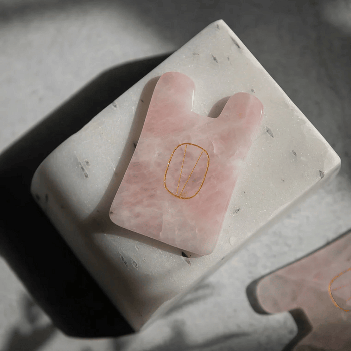 Rose Quartz Gua Sha | Vie Healing facial massage tool made of smooth pink rose quartz stone resting on a textured white surface, promoting skincare and wellness.