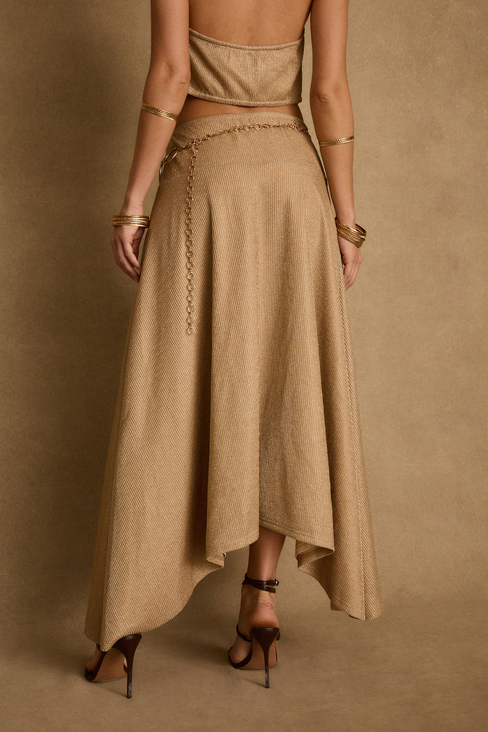 Back view of gold lurex maxi skirt with asymmetrical hem, chain belt and gold bangles.