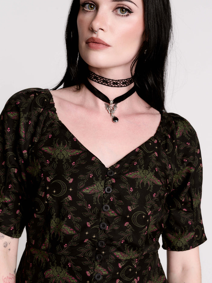 A short-sleeve button-up blouse featuring a dark green and black gothic pattern with pink accents.
