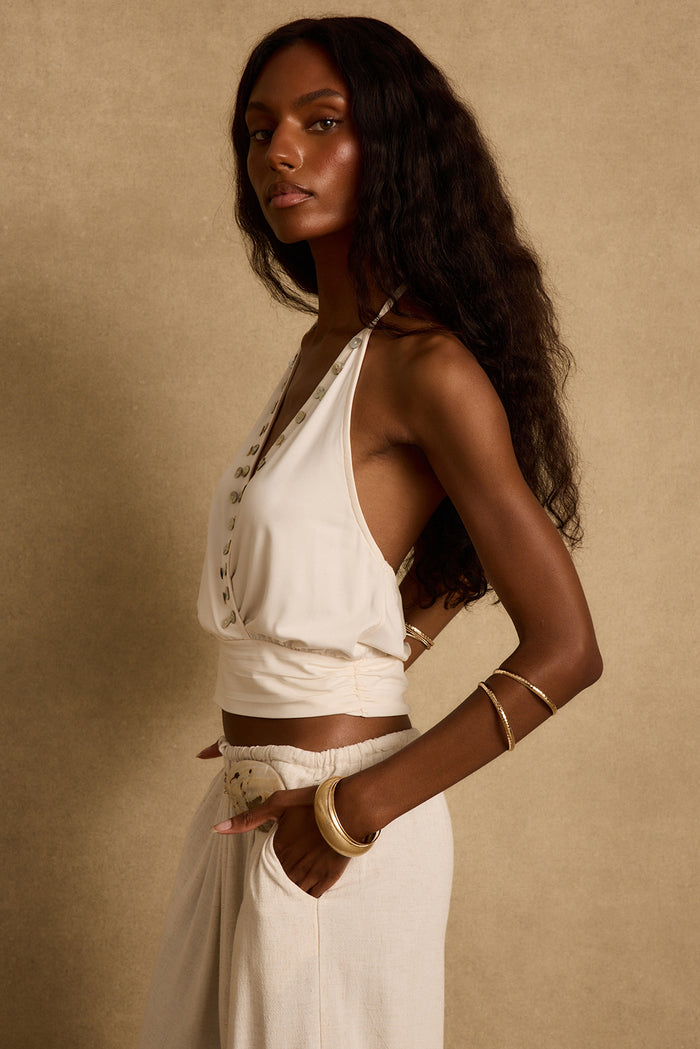 Side profile of the Venice ivory halter top, shell-trimmed plunge neckline styled with linen pants.