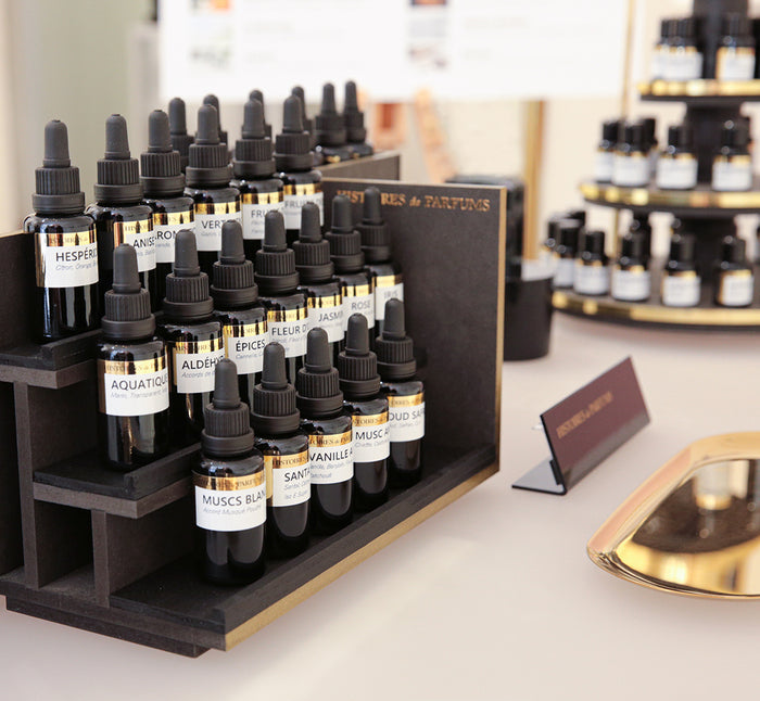 A display of various bottles with black labels and droppers, arranged in rows on a wooden structure, likely to be used for perfume making.