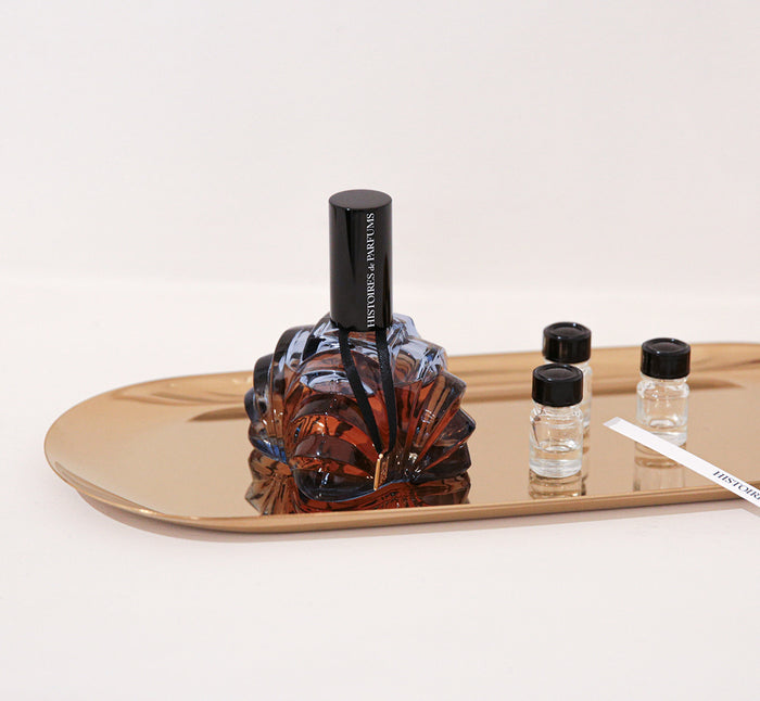 A perfume bottle next to a vial and blotters on a tray.