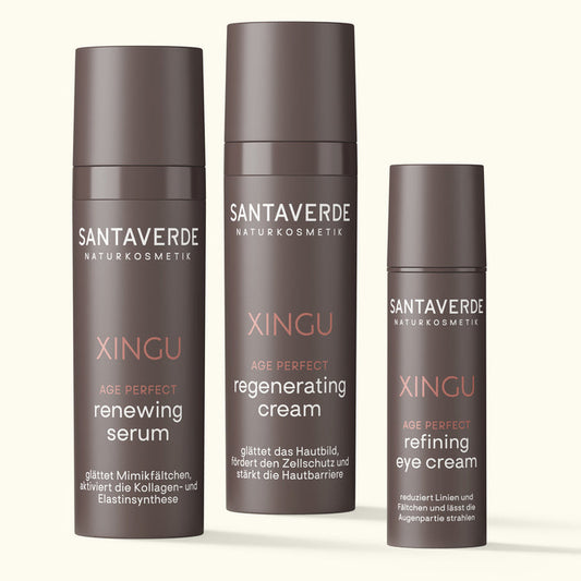 Drei Santaverde XINGU Age Perfect Produkte – renewing serum, regenerating cream und refining eye cream – in braunen Spenderflakons auf hellem Hintergrund nebeneinander stehend.